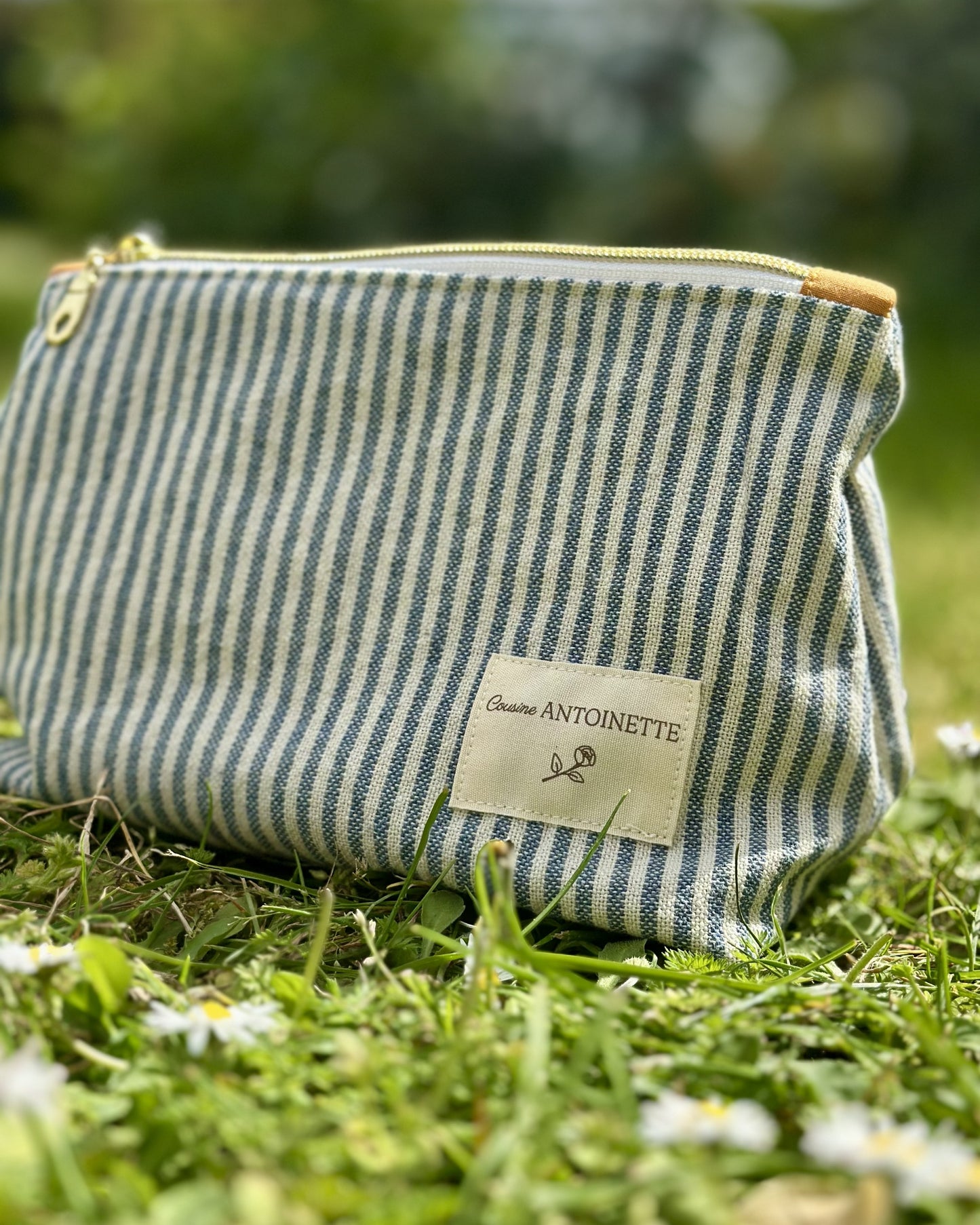 Trousse zippée Deauville Curry posée dans l'herbe avec accessoires – fermeture dorée, coton Oeko-Tex – Cousine Antoinette
