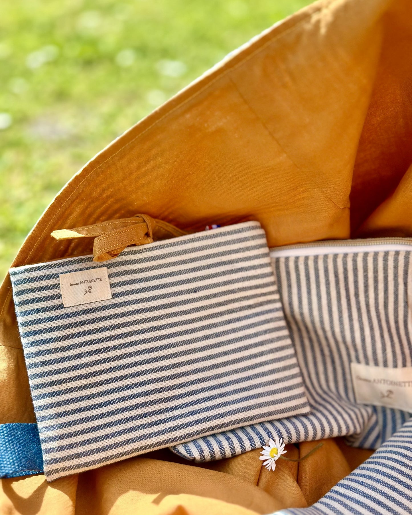 Détail pochette plate et trousse zippée Deauville Curry glissées dans le maxi sac – rayures coton Oeko-Tex bleu et écru, doublure curry, étiquette Cousine Antoinette
